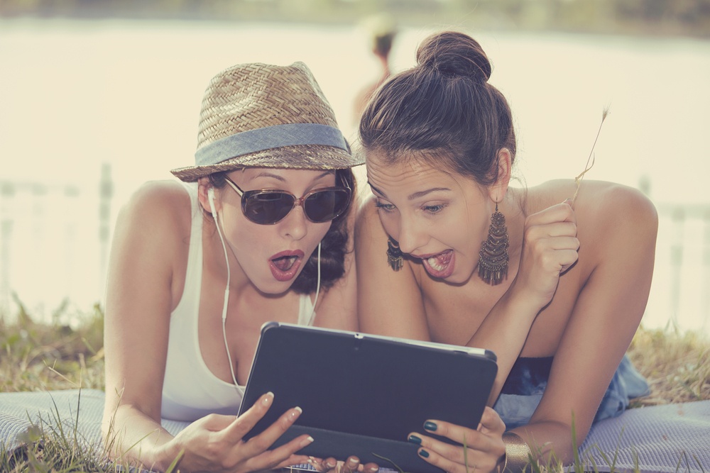 Closeup portrait two surprised girls looking at pad discussing latest gossip news. Young shocked funny women friends reading sharing social media news on mobile pad computer outdoors in park Closeup portrait two surprised girls looking at pad discussing latest gossip news. Young shocked funny women friends reading sharing social media news on mobile pad computer outdoors in park