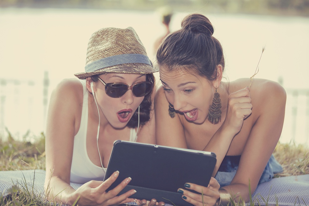 Closeup portrait two surprised girls looking at pad discussing latest gossip news. Young shocked funny women friends reading sharing social media news on mobile pad computer outdoors in park