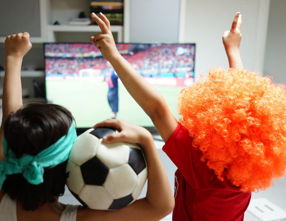 Family with football watching soccer world cup game 2014 on tv in living room